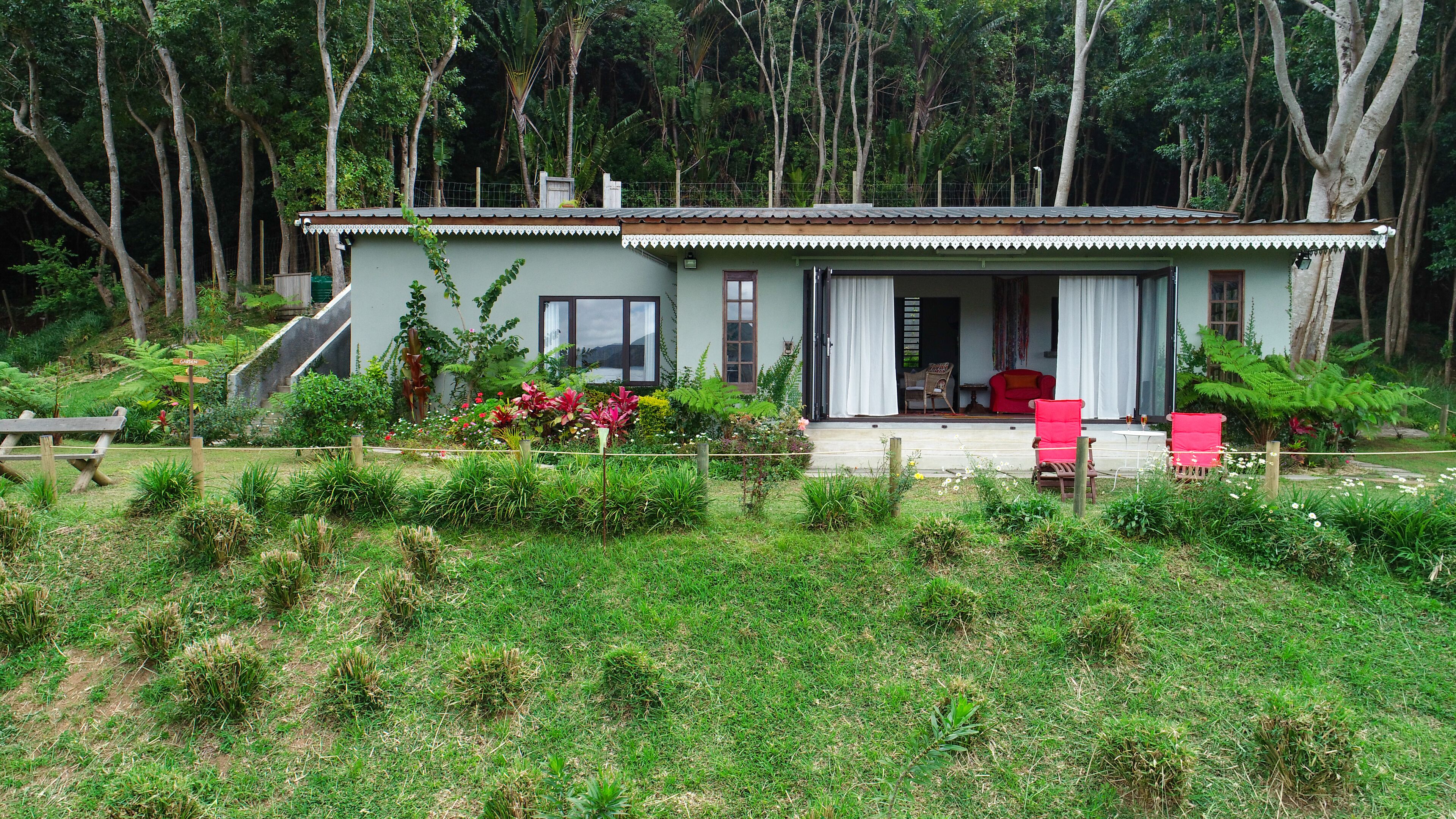 A house with a covered porch, a dining area with a table and chairs, and a garden with various plants and flowers.