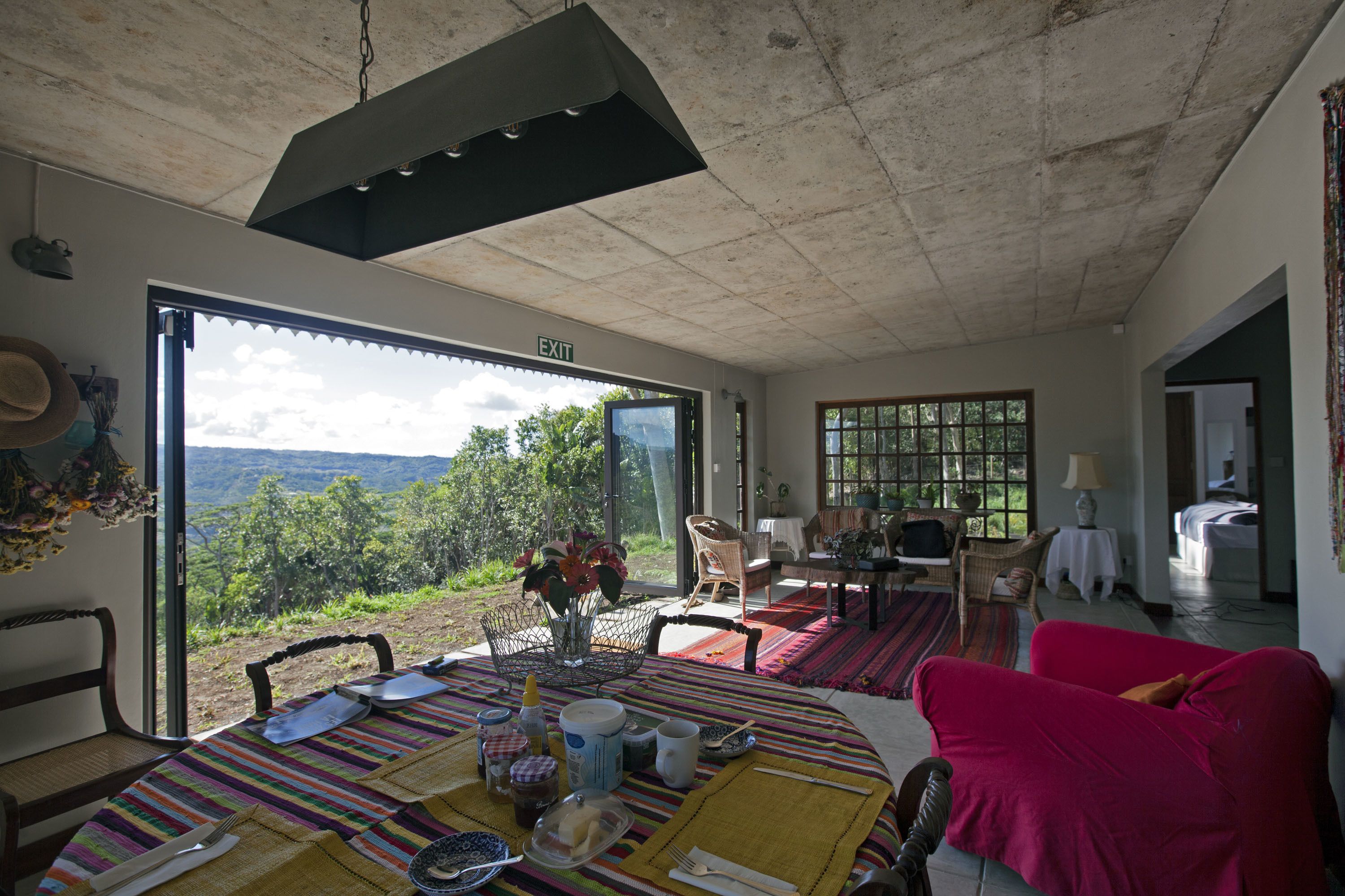 A dining area with a table set for two, a view of the outdoors, and a cozy seating area with a red sofa.