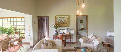 A spacious living room with a high ceiling, a dining area with wicker furniture, and a view through large windows.
