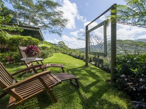 A garden with wooden furniture, a table with a vase of flowers, and a sign indicating a view of mountains. - Green Cottage Chamarel (Chamarel)