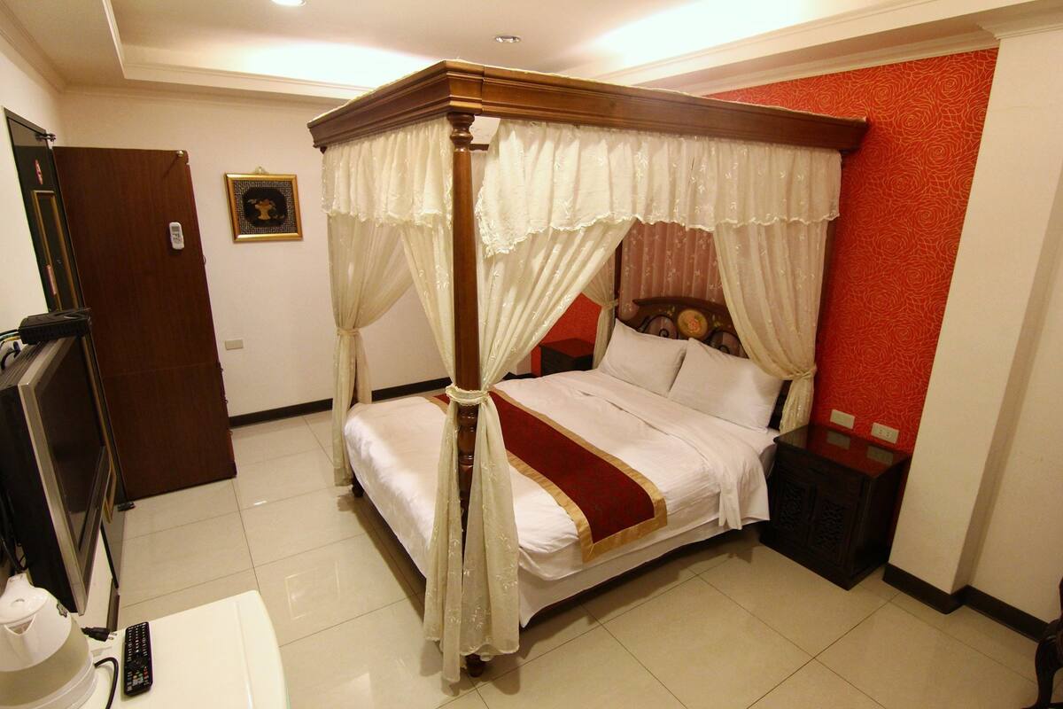 A four-poster bed with a canopy, a bedside table, a nightstand, and a television in a hotel room.