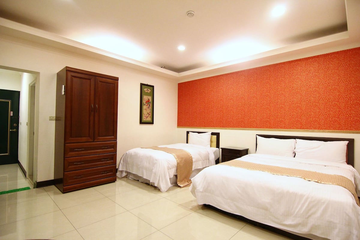 A hotel room with two beds, a wardrobe, and a red patterned wall.