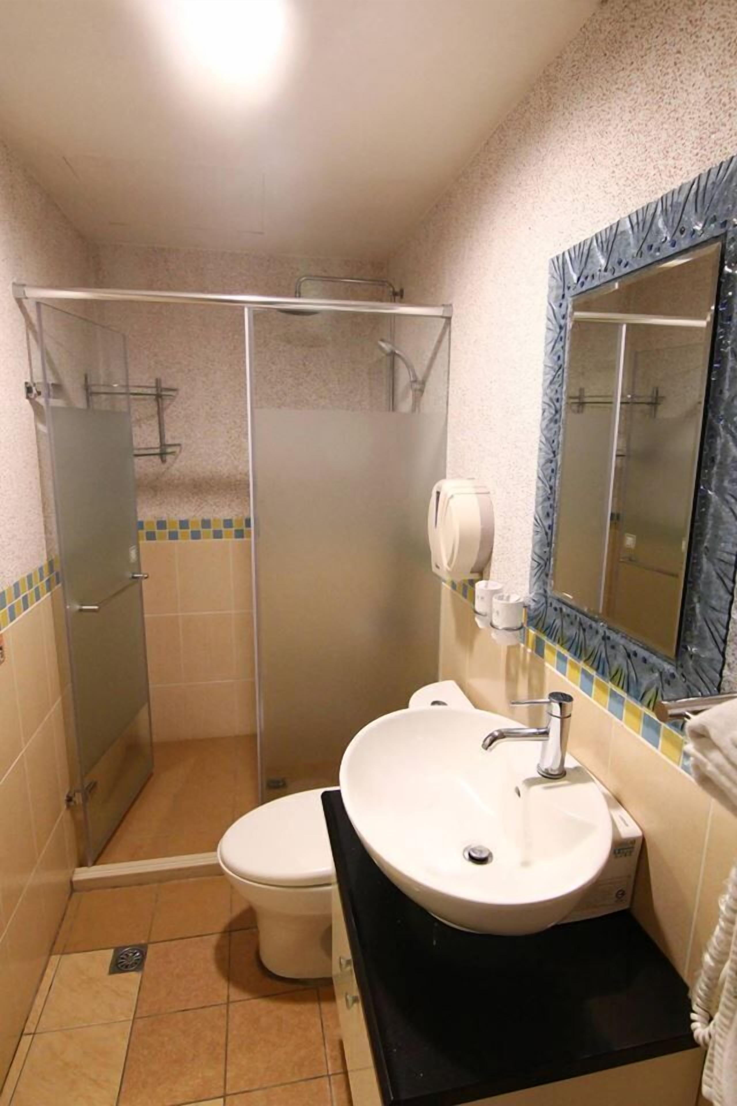 A bathroom with a shower, toilet, sink, and a mirror with a decorative frame.