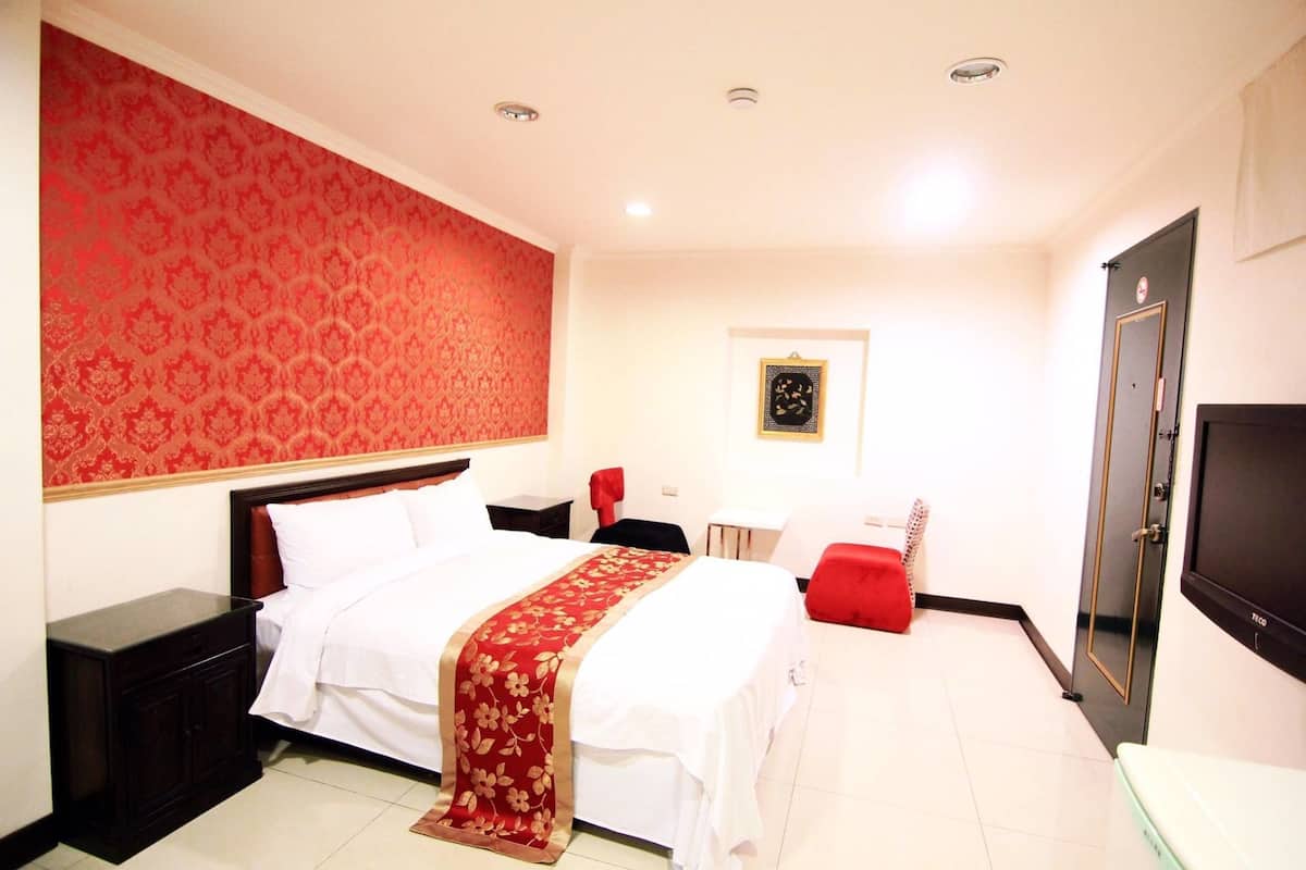 A hotel room with a large bed, a TV, a red wall, and a door.