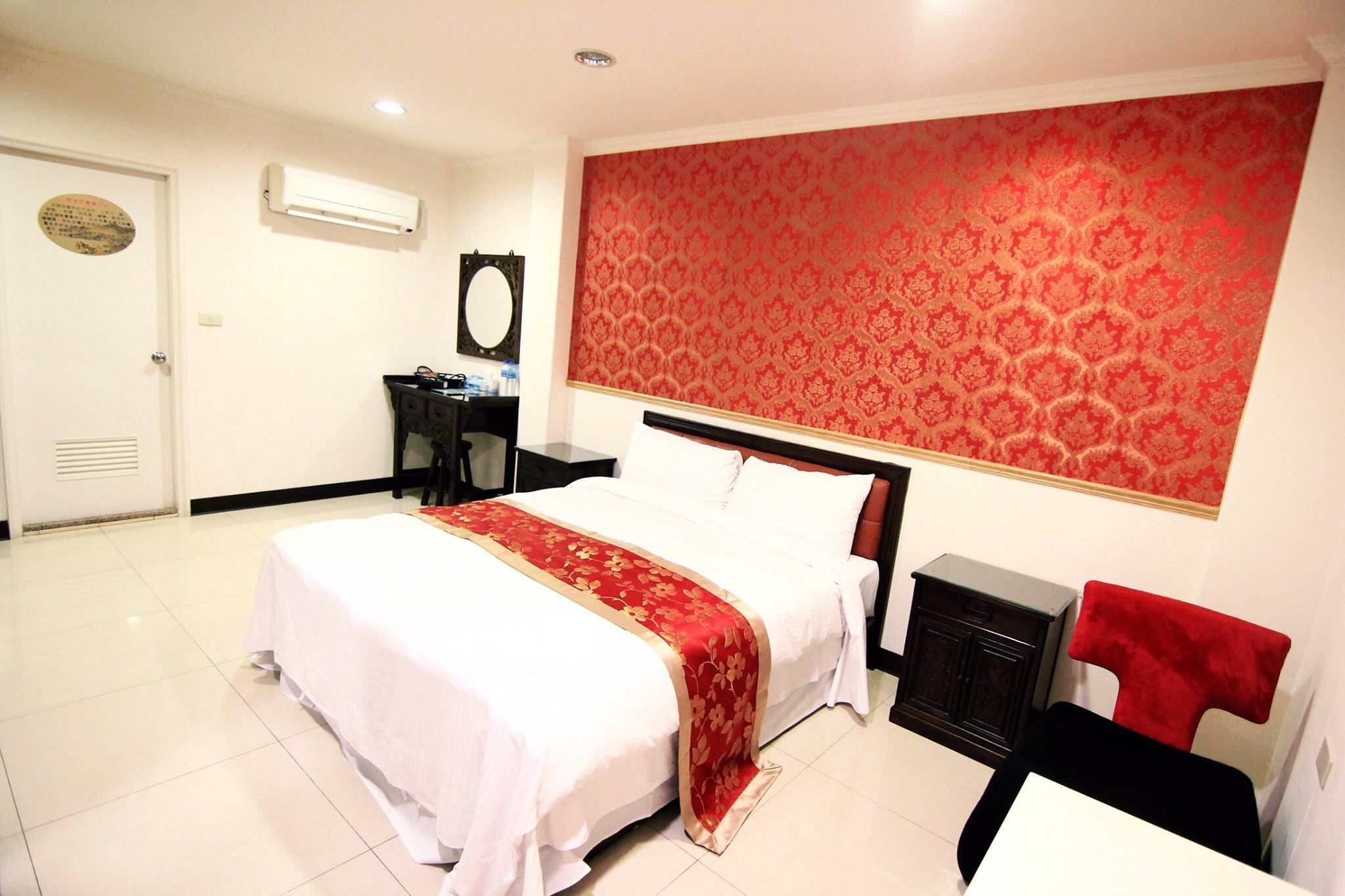 Una habitación de hotel con cama, escritorio, silla y pared con estampado rojo.