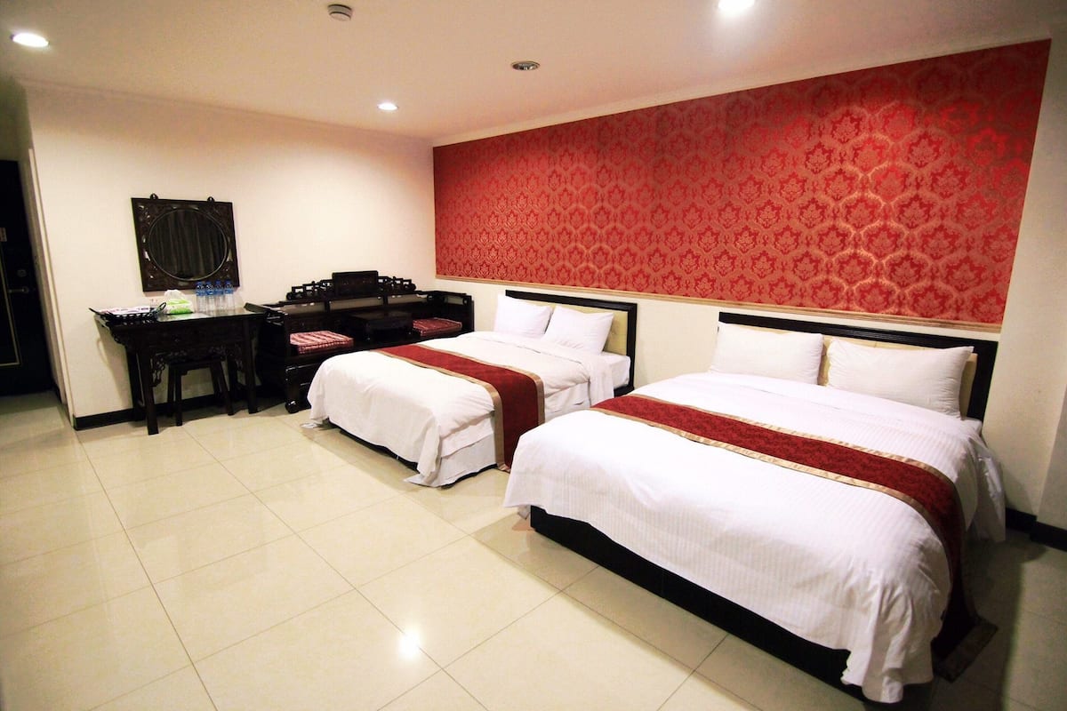 A hotel room with two beds, a desk, and a mirror.
