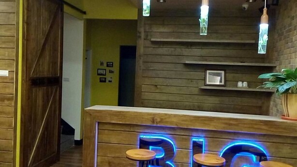 Una zona de recepción con mostrador de madera, un letrero de neón que dice 'BIG' y lámparas colgantes.