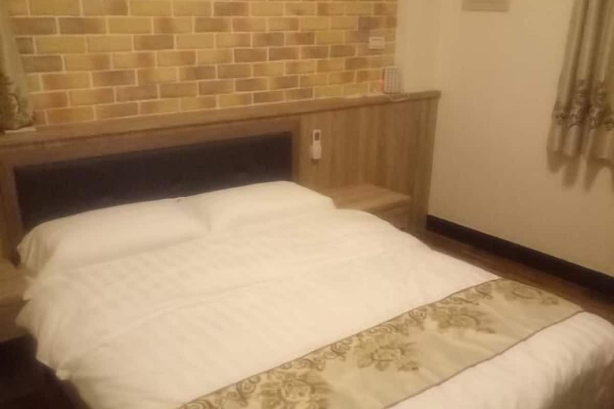 A hotel room with a brick-patterned headboard, a wooden bed frame, and a white bedspread with a patterned runner.