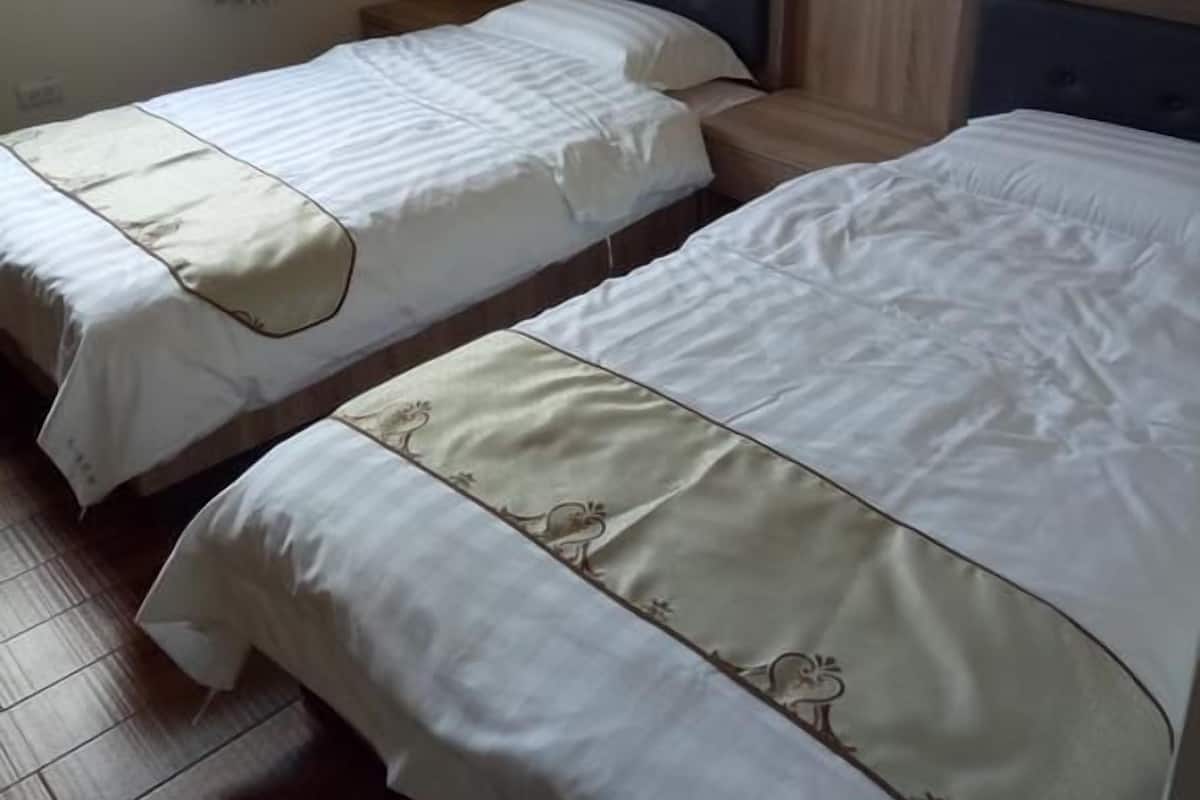 Two single beds with headboards, a brick wall, and a window with curtains.