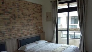 Habitación de hotel con dos camas, una pared de ladrillo, una ventana con cortinas y vistas a edificios.
