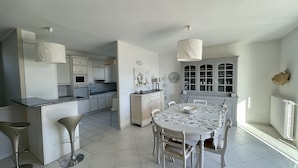 A spacious kitchen with modern appliances, a dining area with a round table, and a large window providing natural light. - Big house with pool house, large garden in a marvelous vacation city (L'isle-Sur-La-Sorgue)