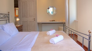 A neatly made bed with white linens and two rolled towels with pink flowers.