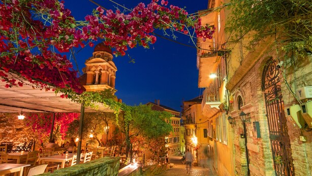 A cobblestone street with a restaurant on one side and a building with a bell tower on the other.