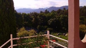 Ein Garten mit Holzpforte, ein hoher Baum und eine bergige Landschaft im Hintergrund.