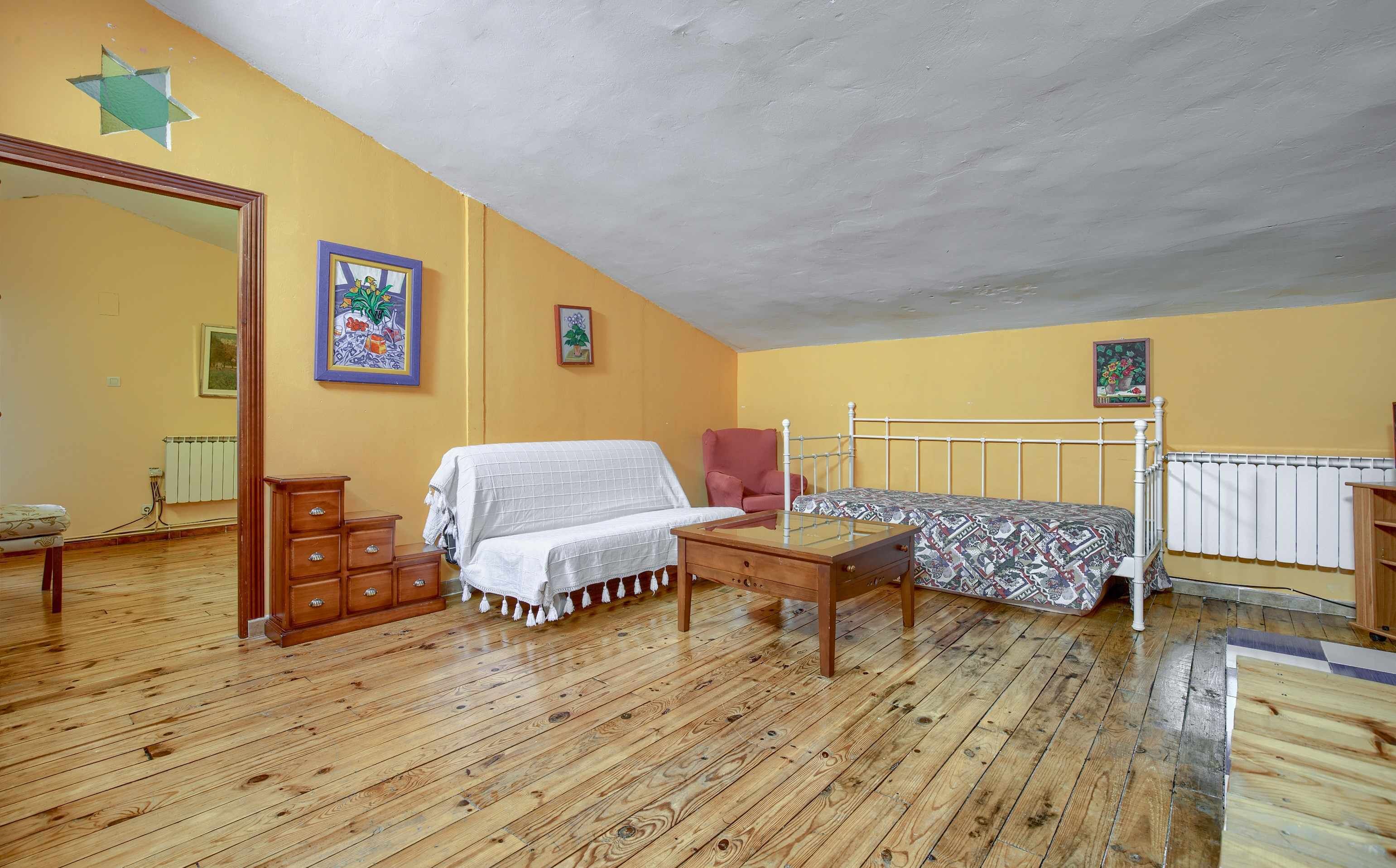 Une chambre avec un plancher en bois, un lit recouvert d’une couvre-lit à motifs, une chaise, une commode et un radiateur.