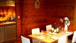 L’intérieur chaleureux d’un chalet en bois comprend une table à manger pour quatre personnes, un coin cuisine et un canapé en cuir.
