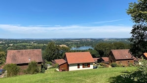 Un cadre rural avec trois maisons situées sur une colline, d’où l’on a une vue sur un lac et la campagne environnante.