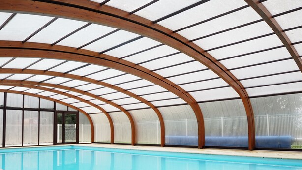 Une piscine intérieure dotée d’un toit en bois aux lignes courbes et de murs en verre.