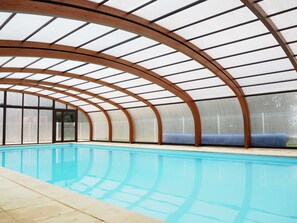 Una piscina interior con techo de madera curva y paredes de vidrio.