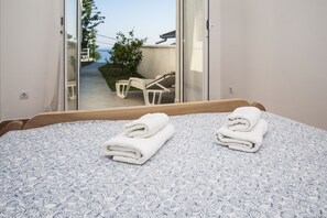 A bedroom with a bed, two towels, and a view of an outdoor seating area with chairs and a plant. - 4 Bed Villa with Swimming Pool and Stunning Sea Views (Podi)