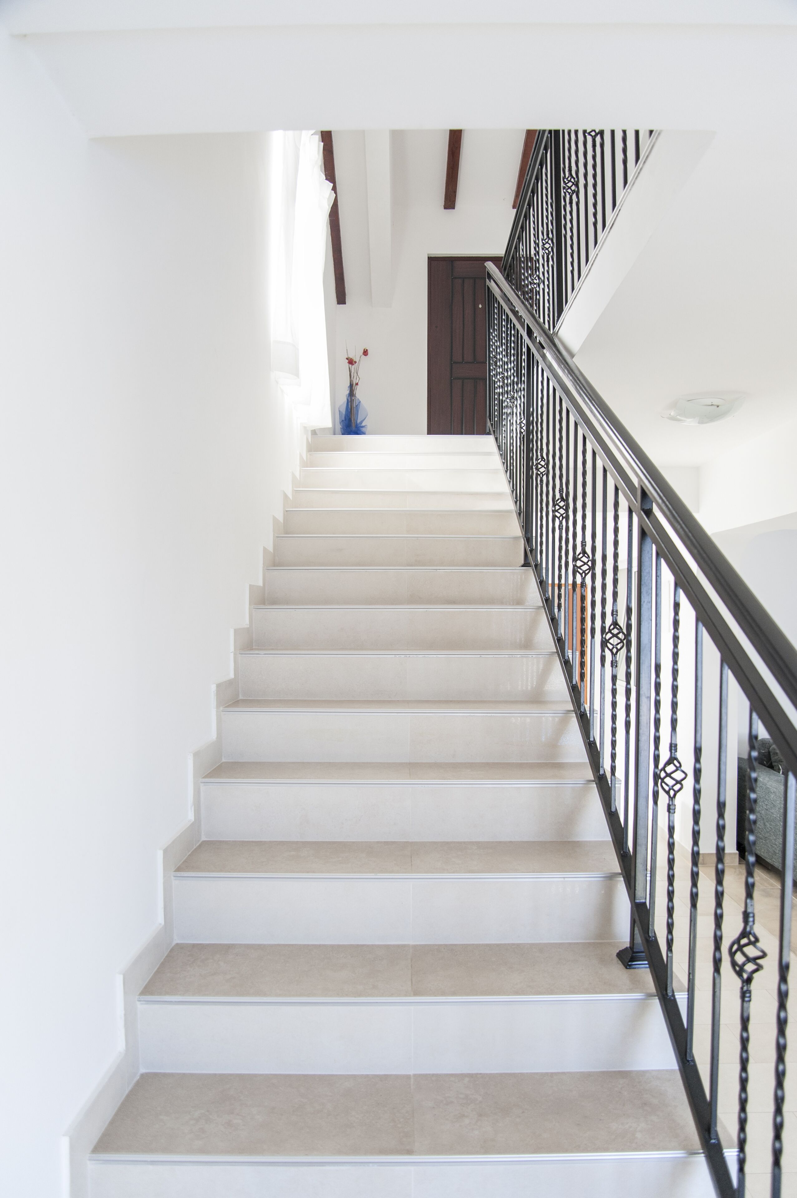 Un escalier avec une rampe blanche et des marches de couleur beige menant à une porte sombre.