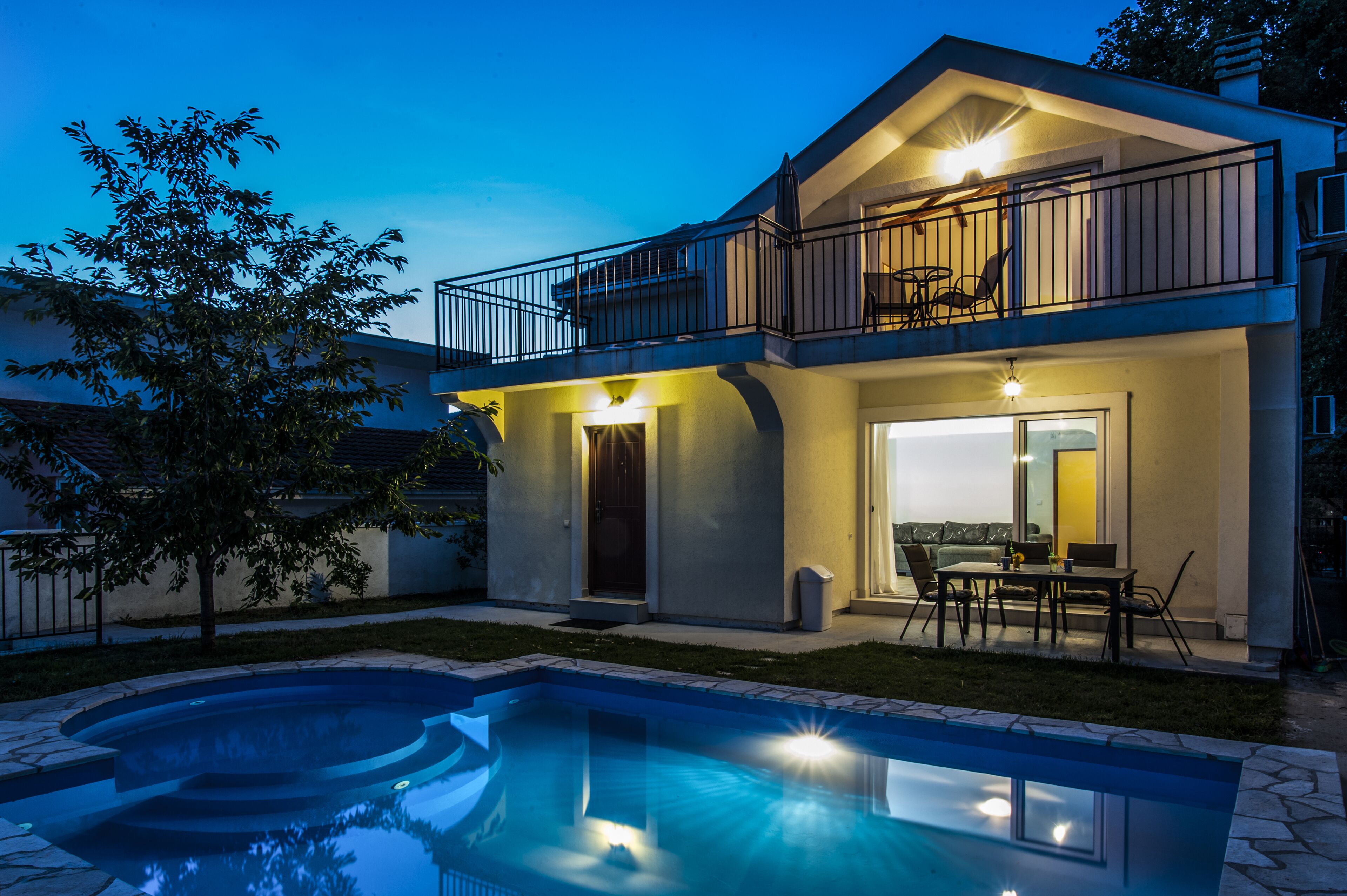 Une maison à deux étages avec un balcon, une piscine et du mobilier d’extérieur.