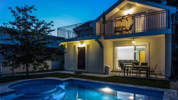 Une maison à deux étages avec un balcon, une piscine et du mobilier d’extérieur.
