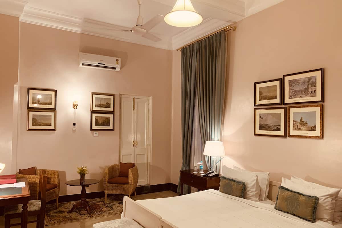 Een hotelkamer met een bed, een bureau, een stoel, een lamp en ingelijste foto's aan de muur.