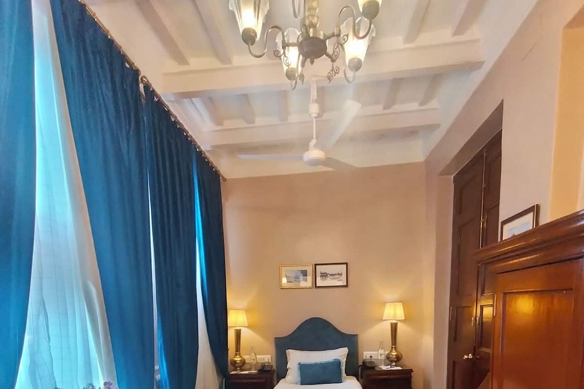 Een hotelkamer met een bed, nachtkastjes, een bureau, een kledingkast en een kroonluchter.
