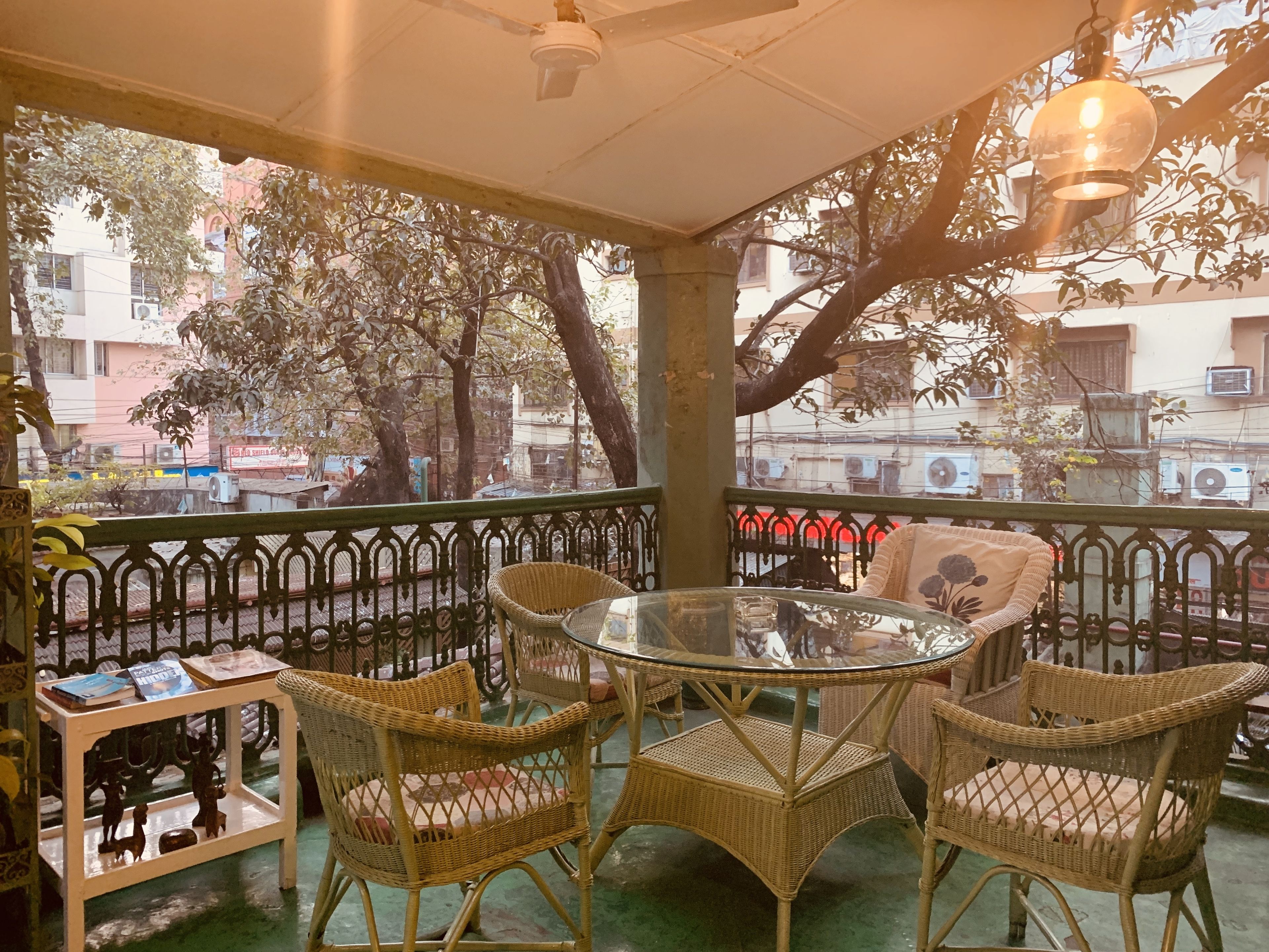 A covered outdoor seating area with wicker furniture, a glass table, and a view of the street and buildings.