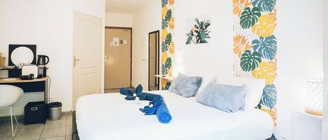 Habitación de hotel moderna con cama, escritorio con cafetera, una silla y un ventanal con estampado de hojas tropicales.