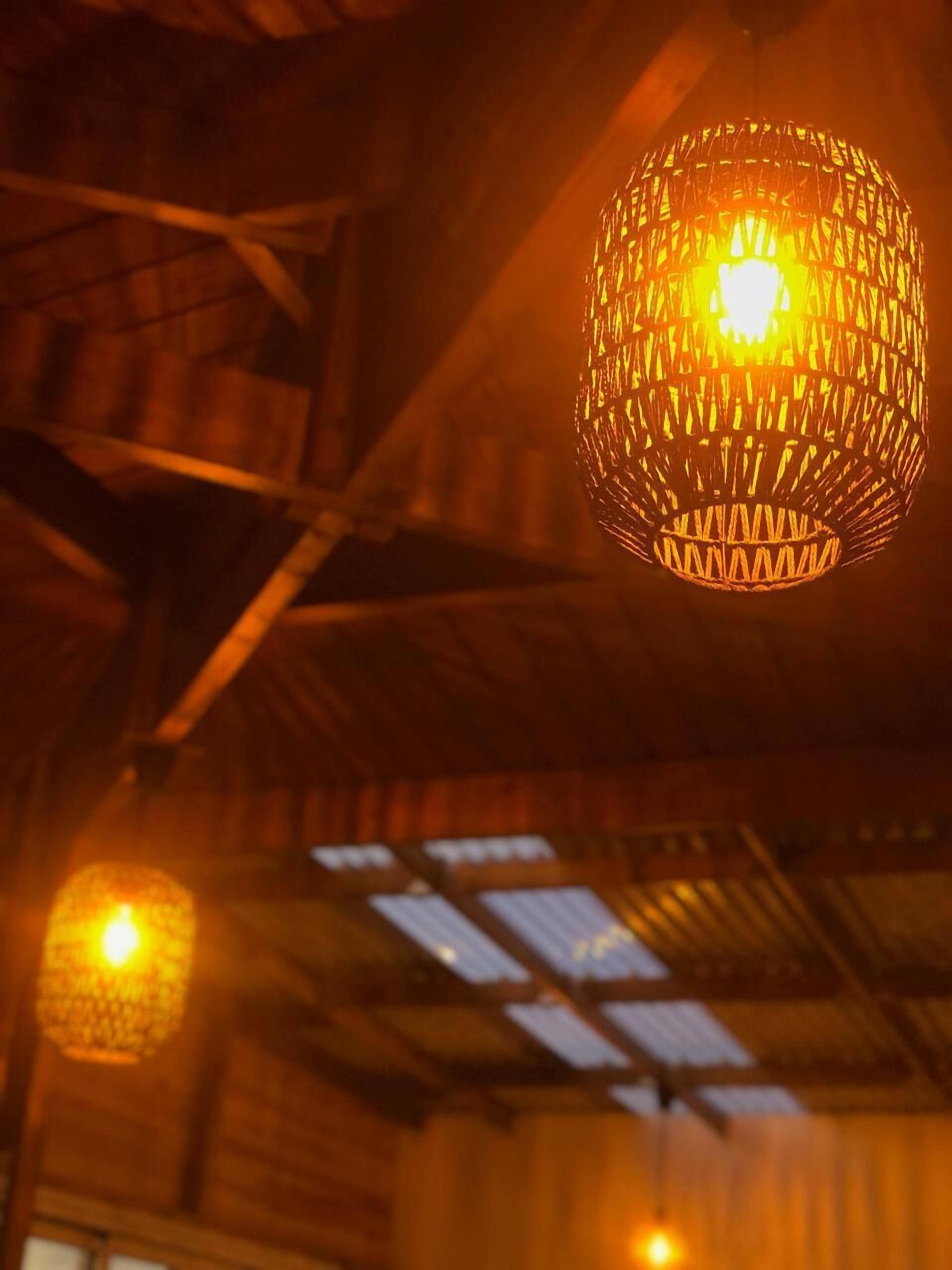 A hanging spherical light fixture with a woven pattern, suspended from a ceiling with visible metal beams.