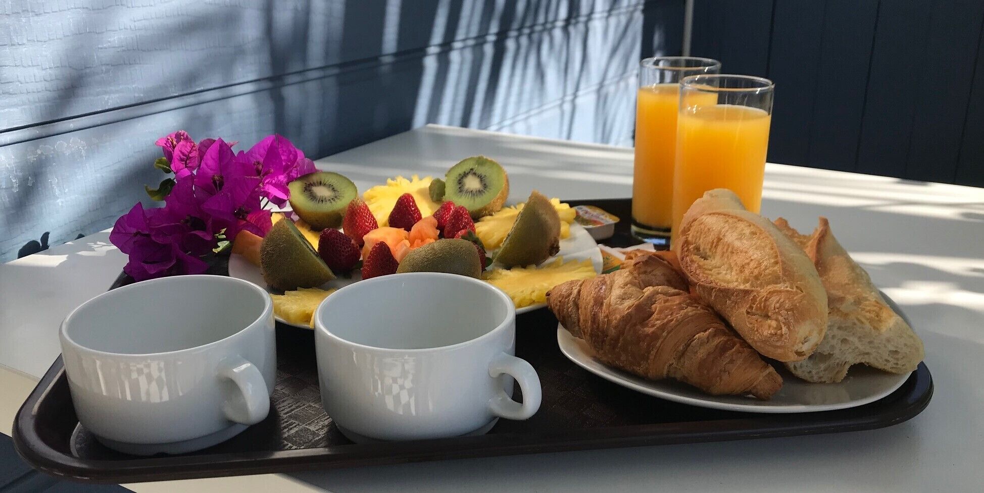 A breakfast tray with croissants, fruit, and juice glasses on a table.