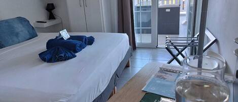 A hotel room with a bed, a nightstand, a table with a glass of water, a book, and a view of the outside balcony.
