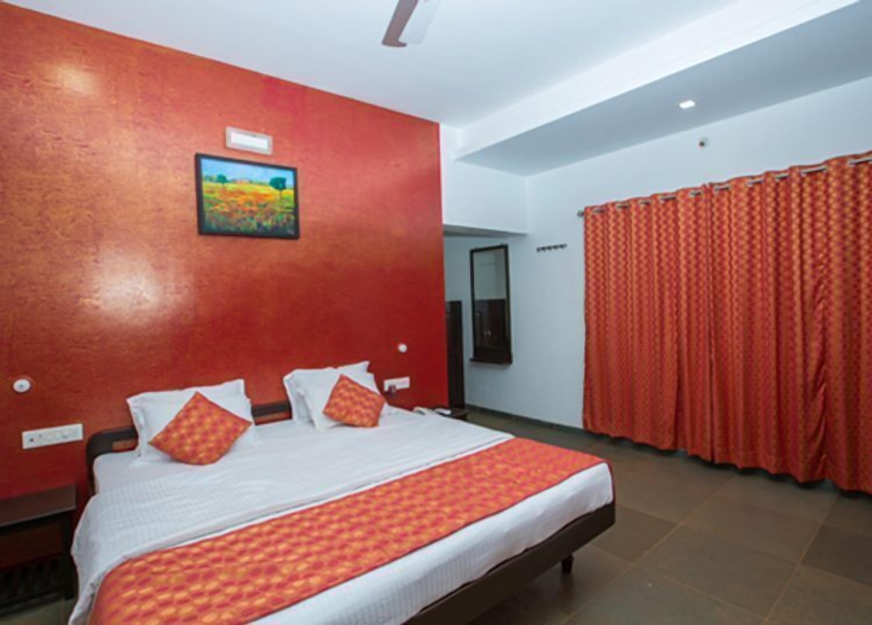 A hotel room with a large bed, red curtains, and a painting on the wall.