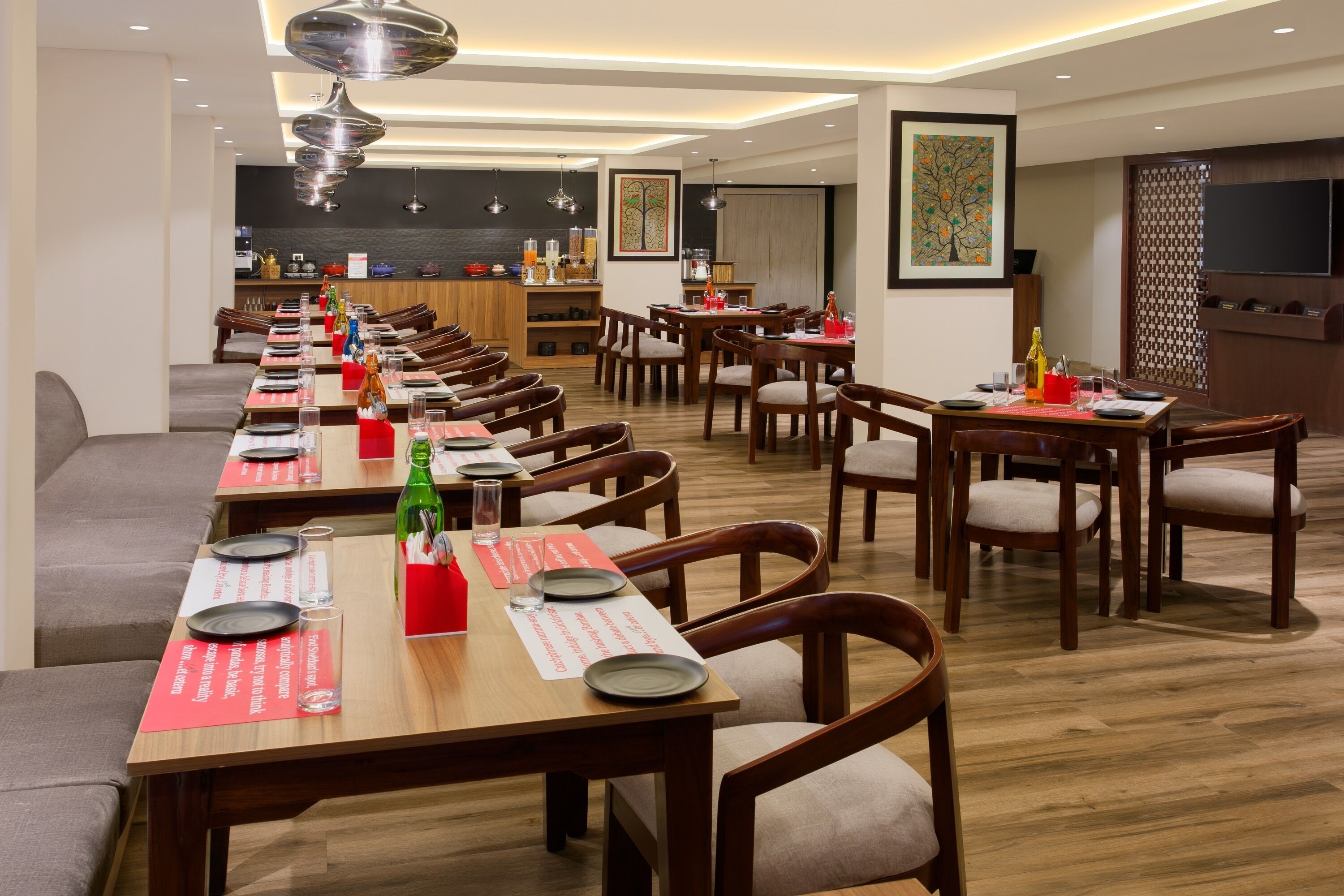Un grand espace dédié à la salle à manger, avec plusieurs tables et chaises, une cuisine à l’arrière-plan et des œuvres d’art accrochées aux murs.
