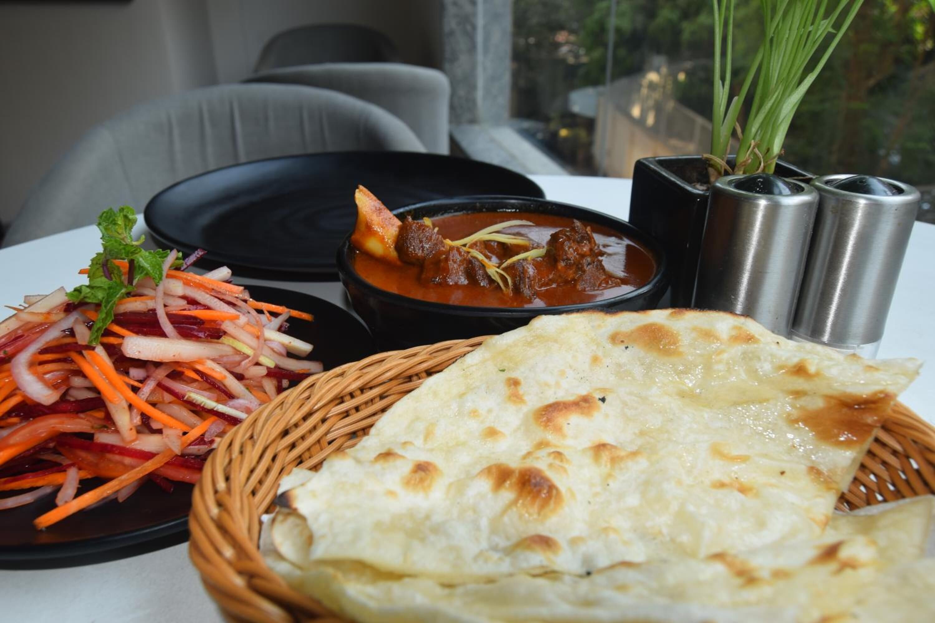 Une table dressée avec un repas composé d’un ragoût, d’une salade et de pain plat.