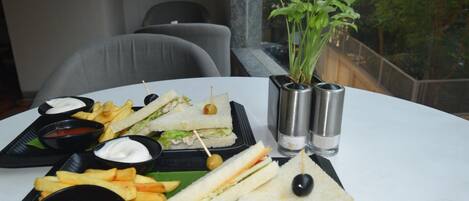 A table with a sandwich, fries, and dipping sauces, with a plant and salt and pepper shakers in the background.