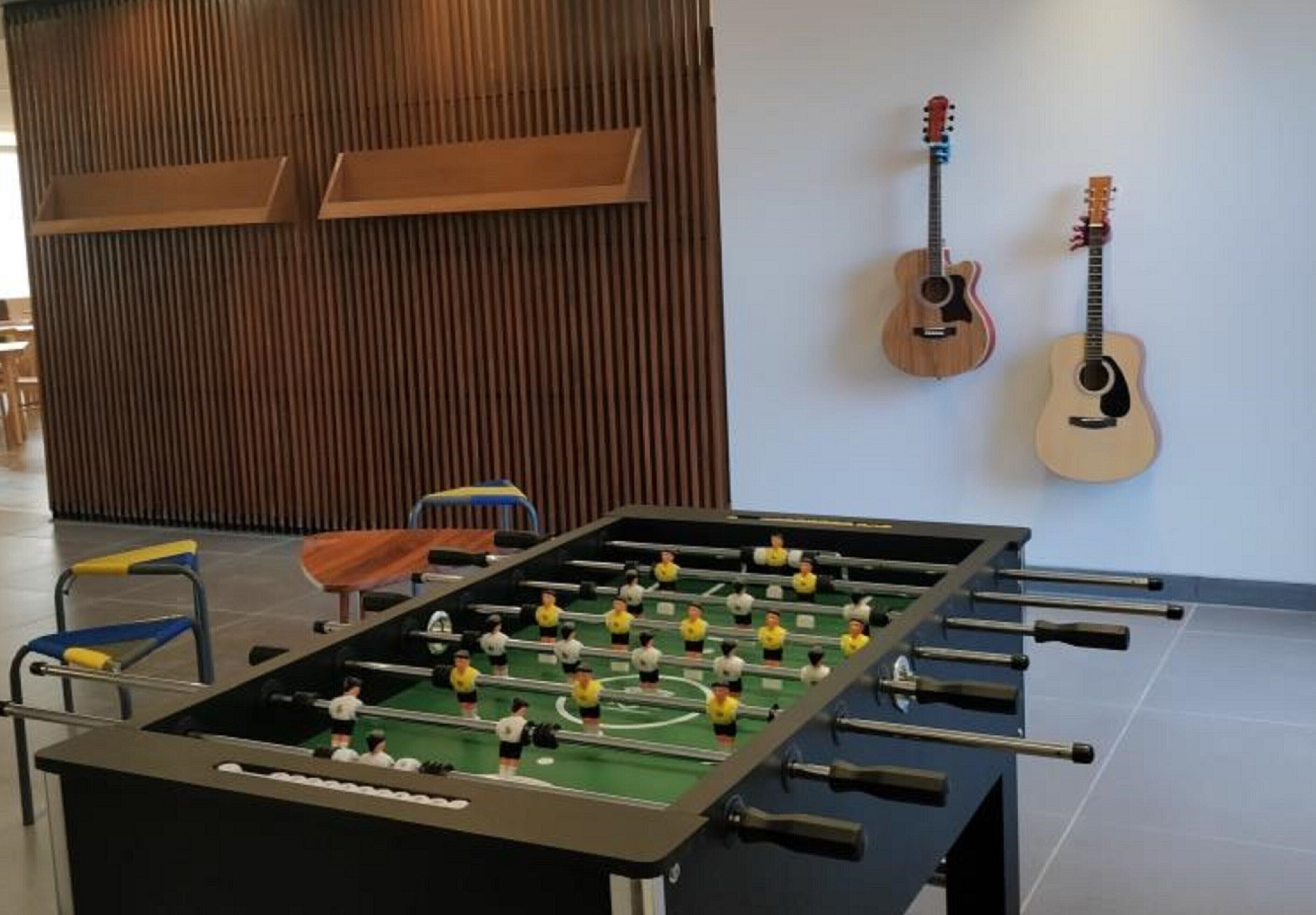 A foosball table in a room with wooden paneling and two guitars on the wall.