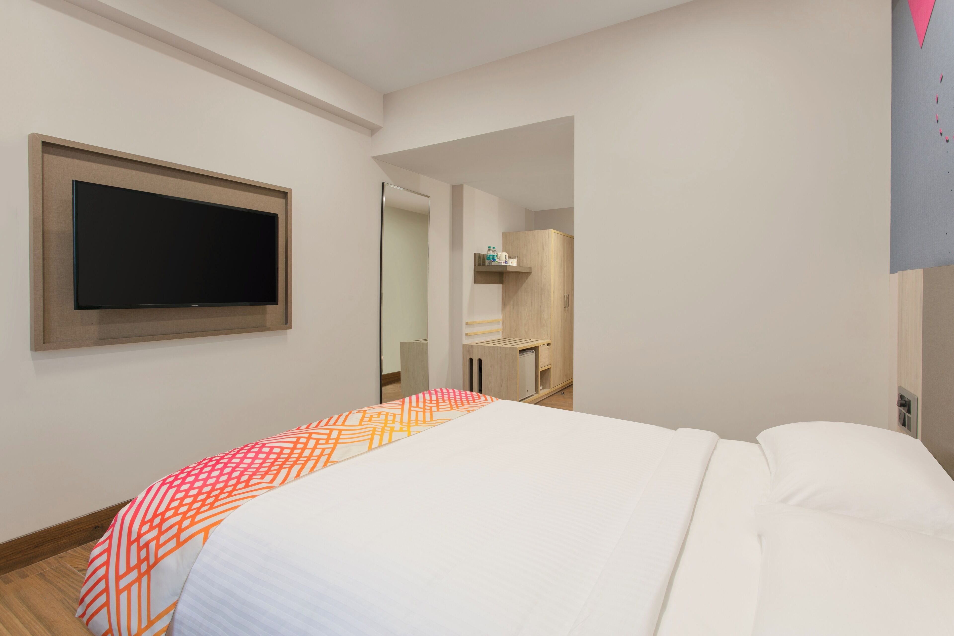 A hotel room with a bed, a flat-screen TV mounted on the wall, a walk-in closet, and a bathroom with a mirror and towel rack.