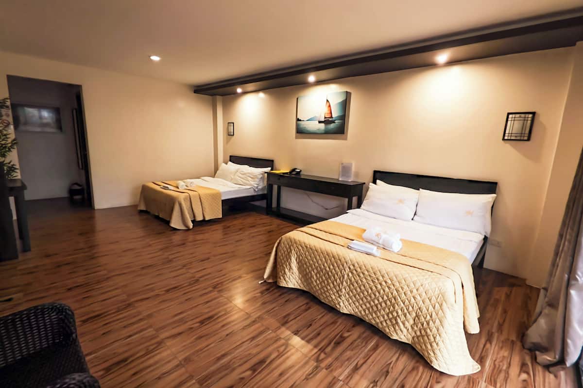 A hotel room with two beds, wooden flooring, a nightstand, a desk, and a painting on the wall.