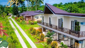 A two-story building with a balcony, surrounded by well-maintained gardens and palm trees. - A&A Garden Suites (Amadeo)