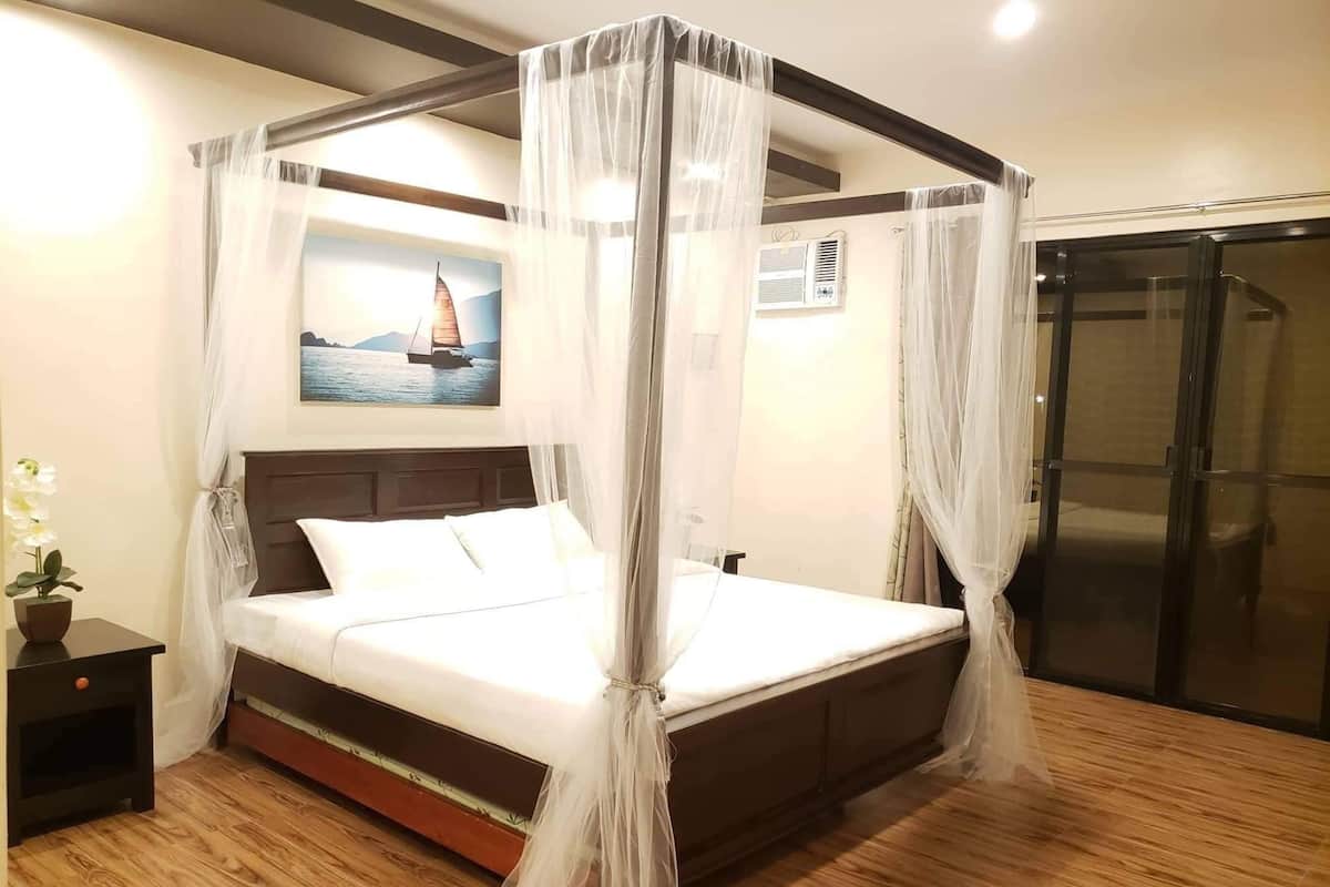 A four-poster bed with a canopy, a nightstand with a plant, a painting of a sailboat, and a sliding door.
