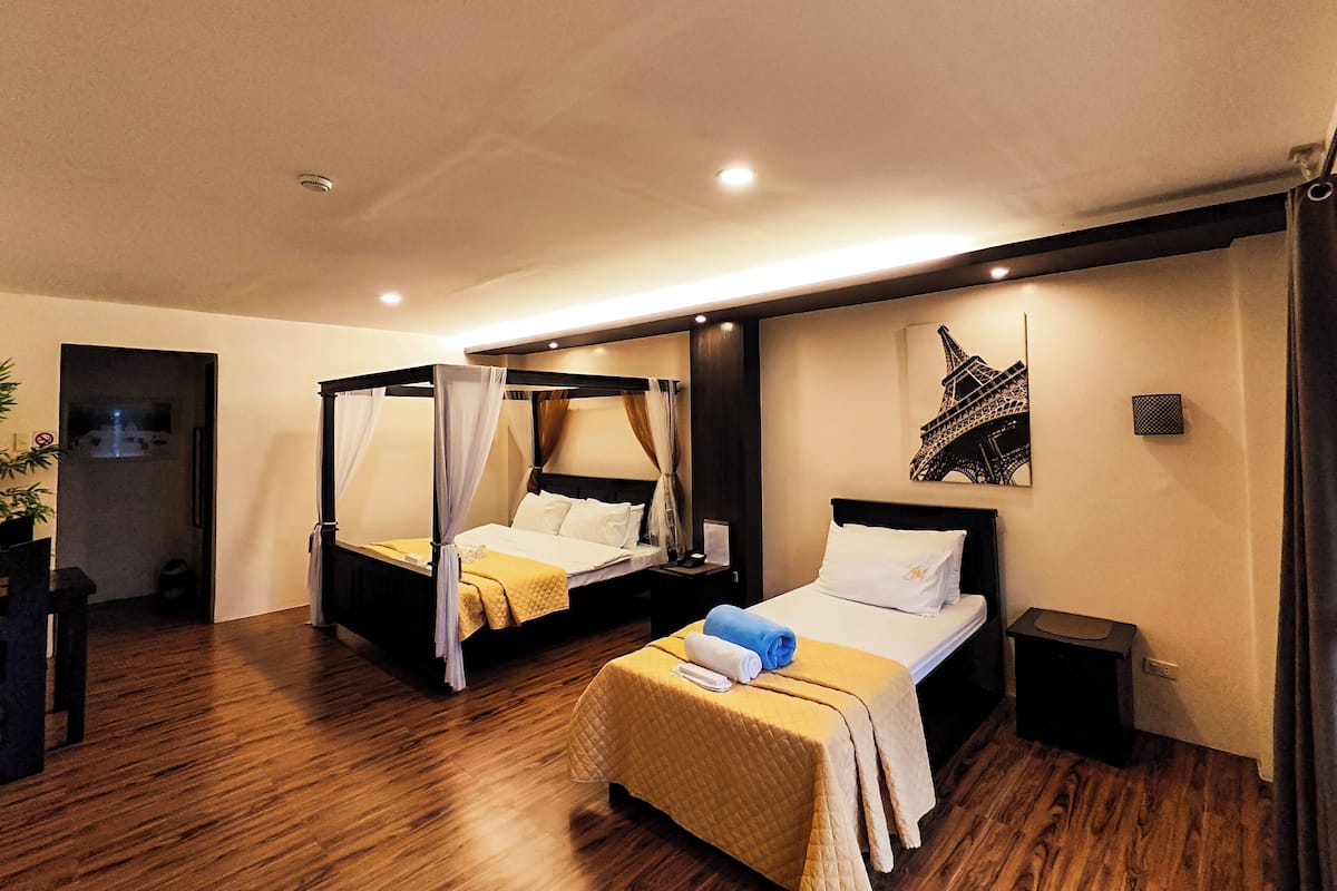 A hotel room with two beds, a nightstand, a small table, and a wall-mounted picture of the Eiffel Tower.