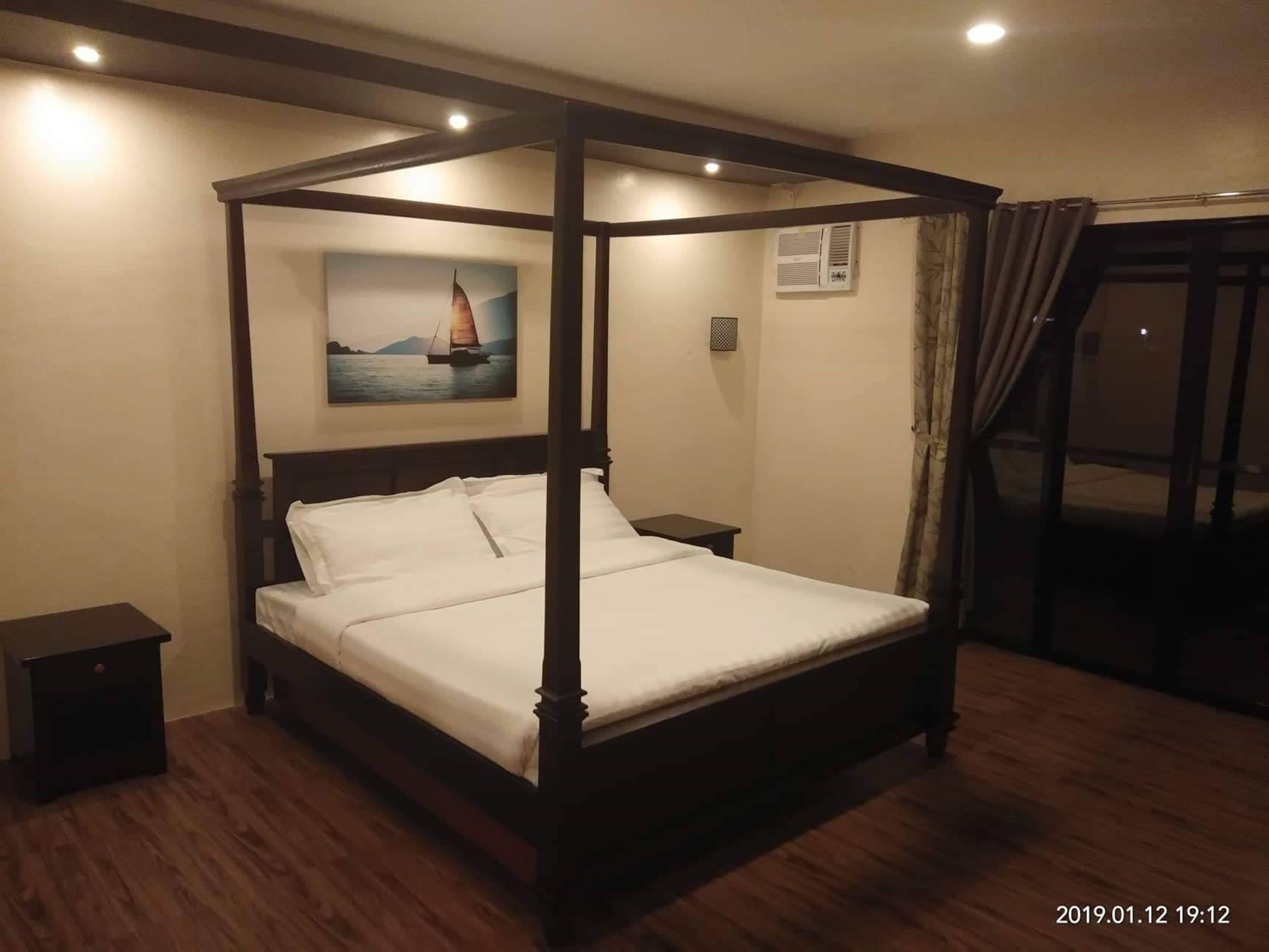 A four-poster bed in a hotel room with a painting of a sailboat on the wall.