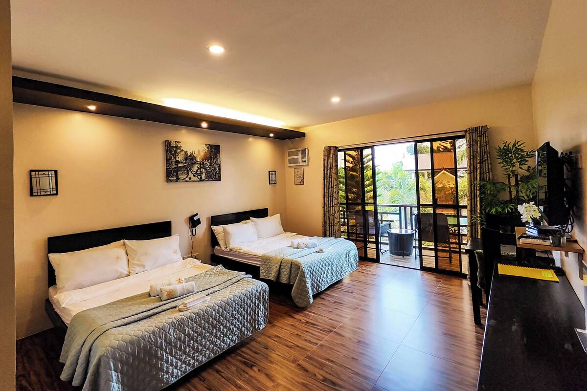 A hotel room with two beds, a large sliding glass door leading to a balcony, and a television on a stand.