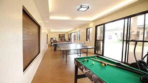 A billiards room with a pool table, a table tennis table, and a window with a view of the outside. - A&A Garden Suites (Amadeo)