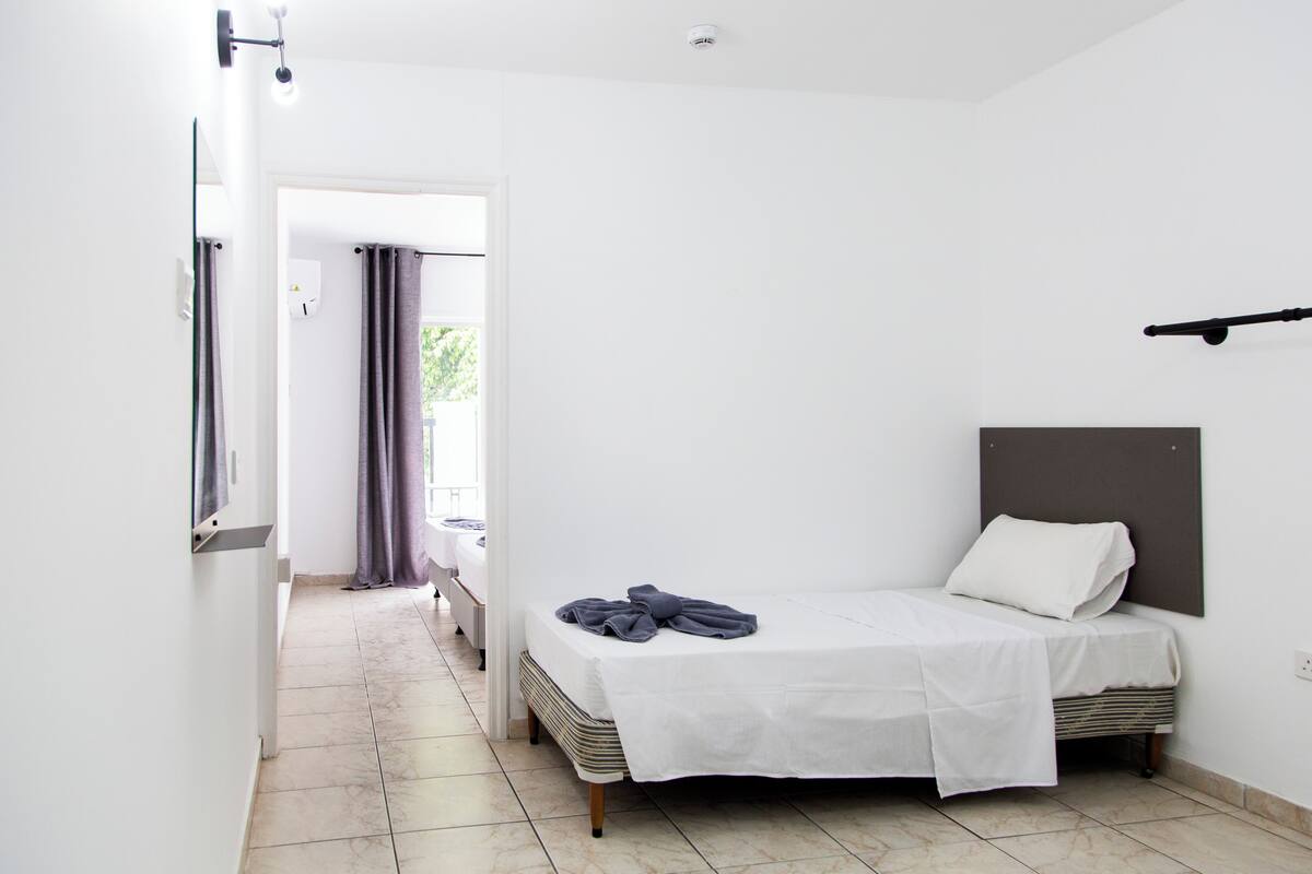 Habitación de hotel con una cama individual, cabecera, mesita de noche y vistas a un balcón.