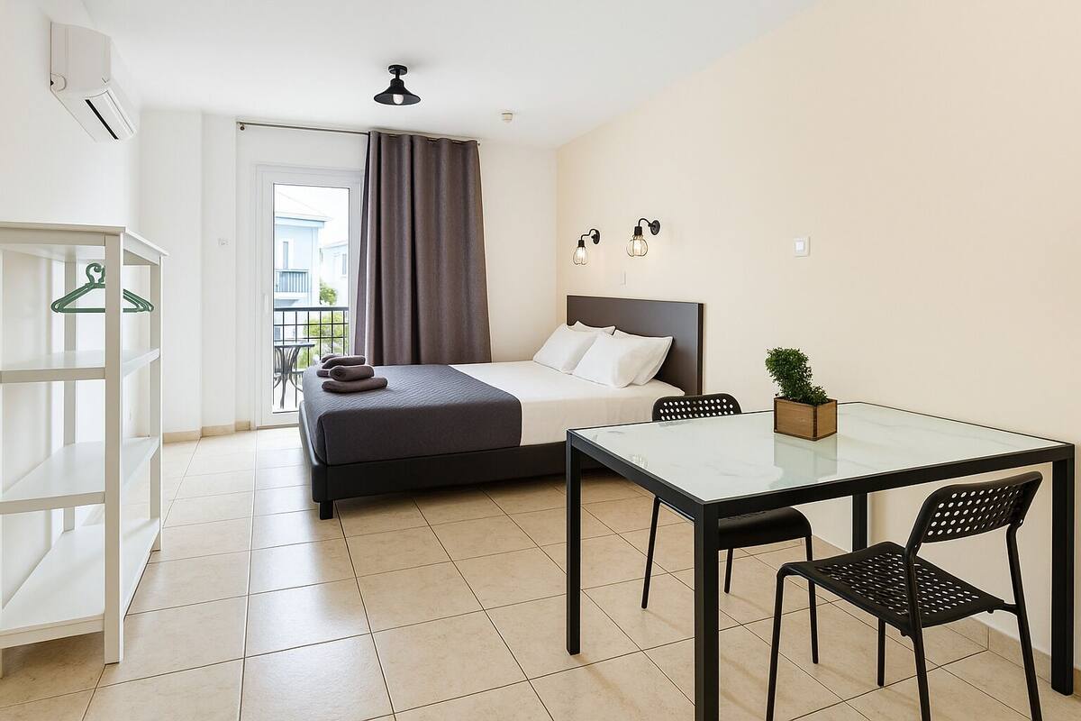 Habitación de hotel con cama, una mesa y sillas, una planta colgante y vistas al exterior.
