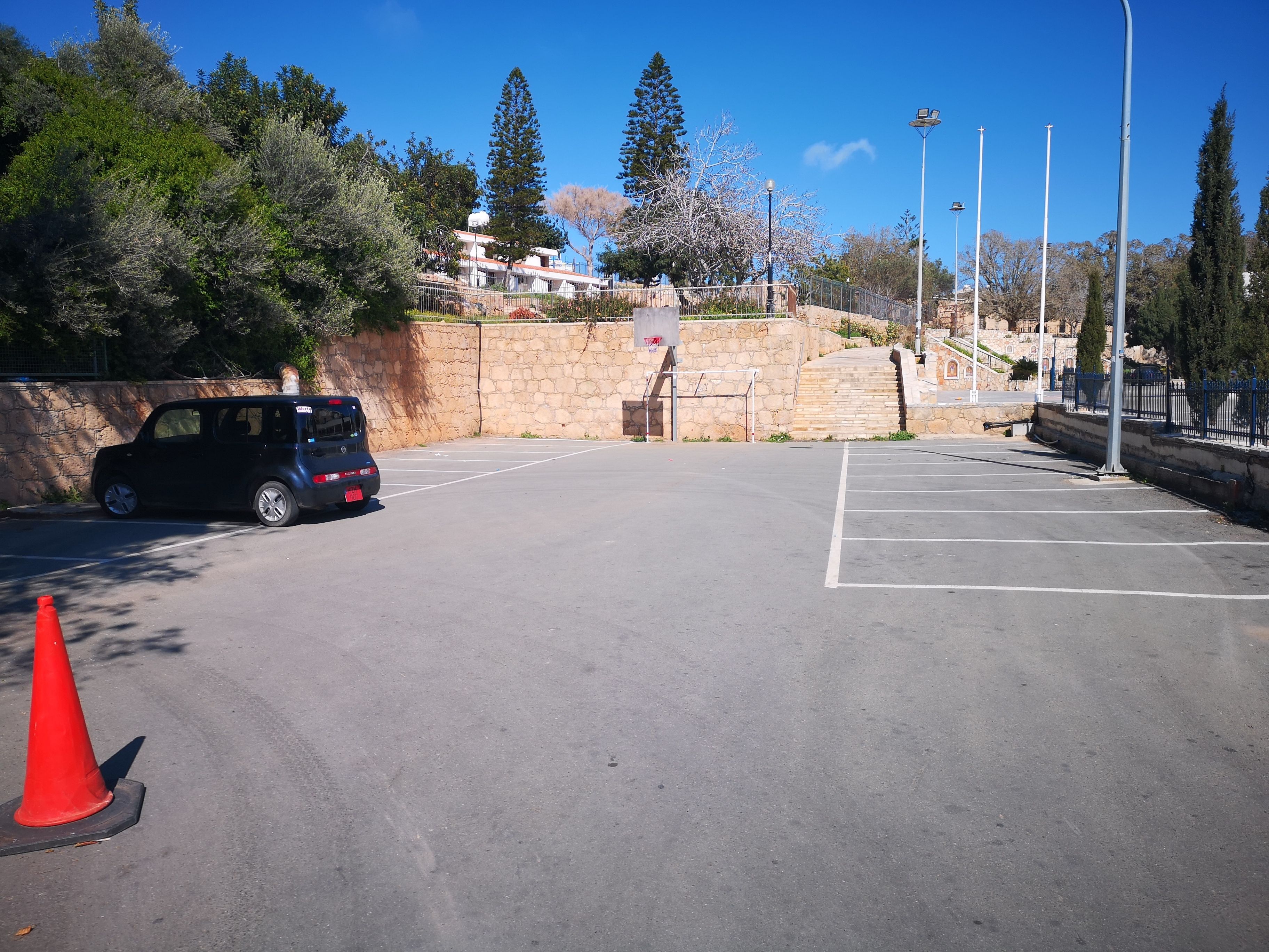 A parking area with a car, a stone wall, and a staircase leading to a building.